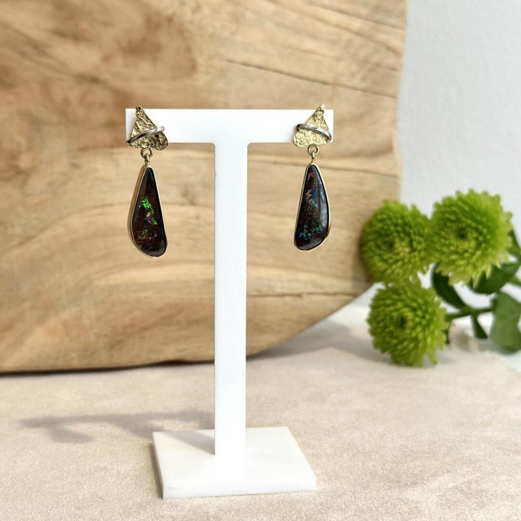 Handgefertigte Opal-Ohrgehänge aus 585er Gelb- und Weißgold, gefertigt von einem Goldschmied, präsentiert auf einem Schmuckaufsteller vor einem Holzhintergrund.“ Hochwertige Juwelierarbeit aus Wien mit Edelsteinen.