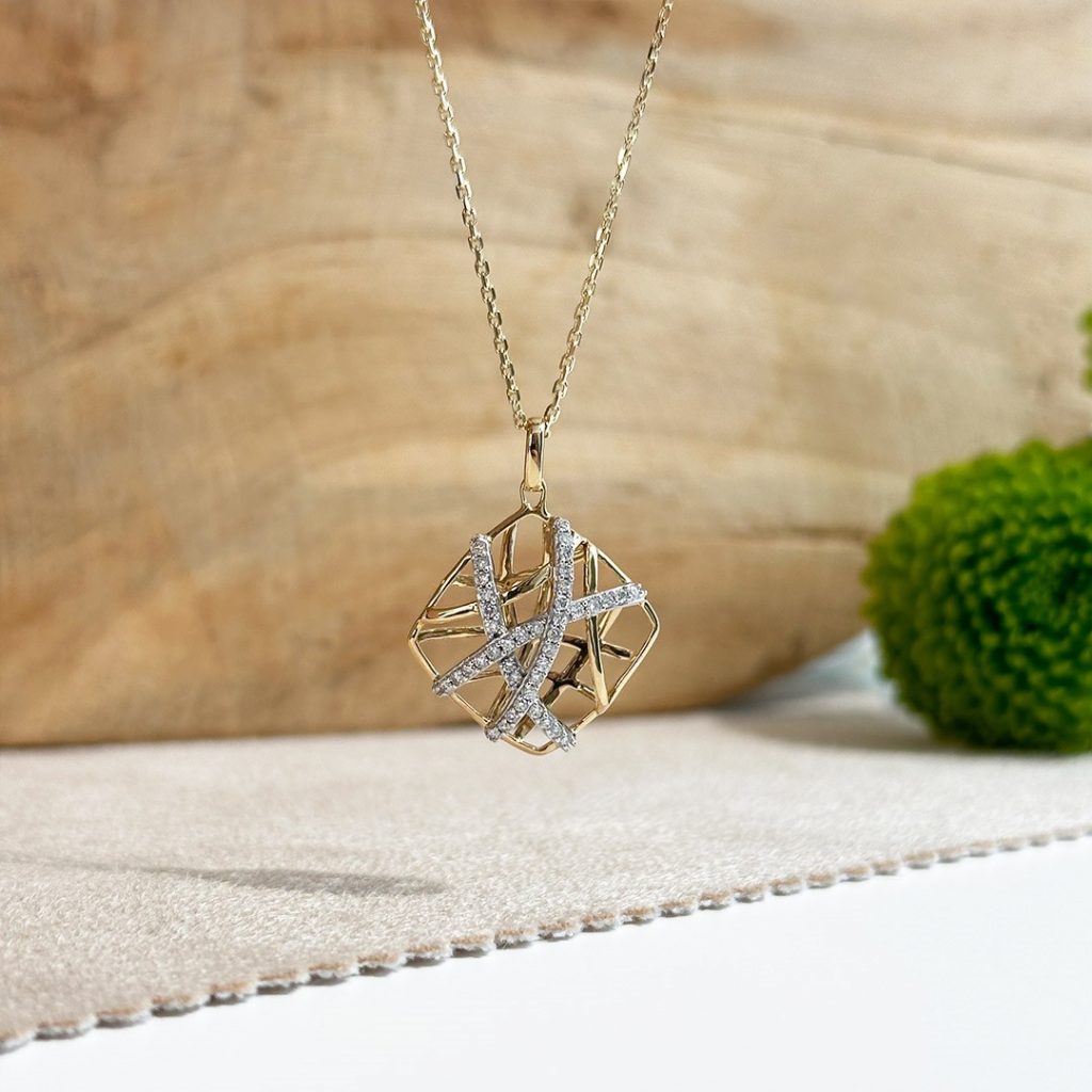 Nahaufnahme eines durchbrochenen Diamantanhängers in 585 Gold auf Goldkette vor Holzhintergrund.