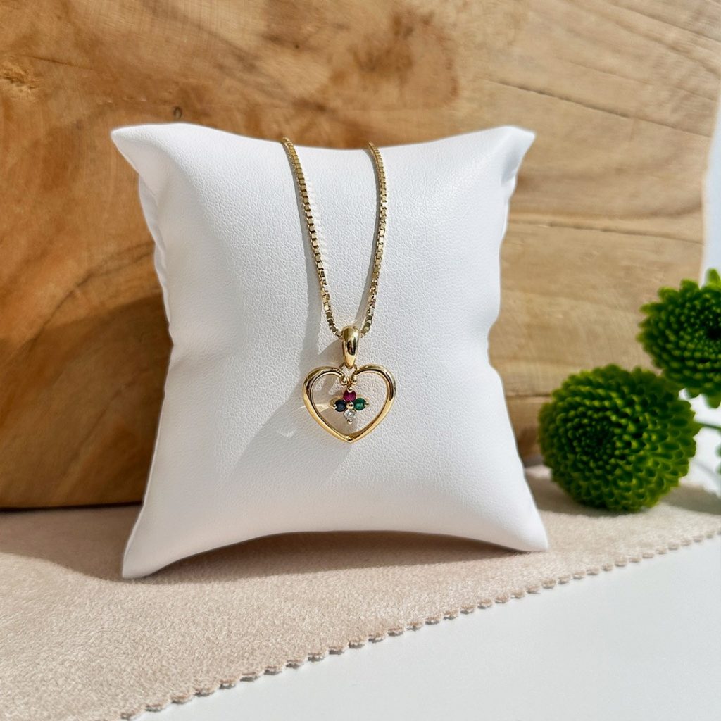 Herzanhänger aus 585 Gelbgold mit Diamant und Farbsteinen Saphir, Rubin, Smaragd auf einer Goldkette präsentiert auf einem Schmuckpolster und vor einem eleganten Holzhintergrund 15570
