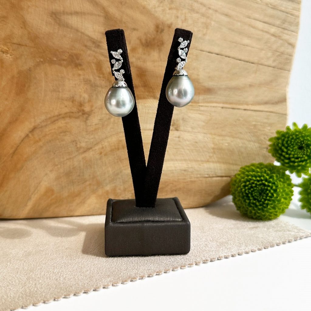 Juwelier Wien - Juwelier Silvia Brandstetter: Elegante Diamantohrringe aus 750er Weißgold mit 0,82 Karat Navette- und Brillantschliff-Diamanten. Abgerundet mit einer edlen grauen Tahitiperle für eine weiche Note. Präsentiert auf einem Ohrständer in Nahaufnahme vor einer Holzwand.