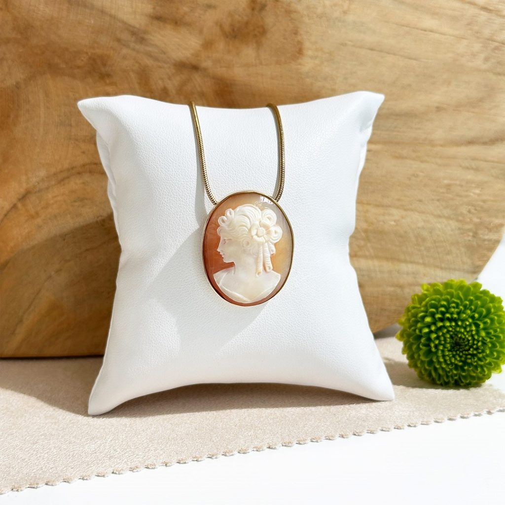 Kamee Goldanhänger aus 585 Gelbgold mit schlichter Fassung, präsentiert auf einem weißen Schmuckpolster vor einer Holzwand mit grünem Blümchen als Kontrastdetail.