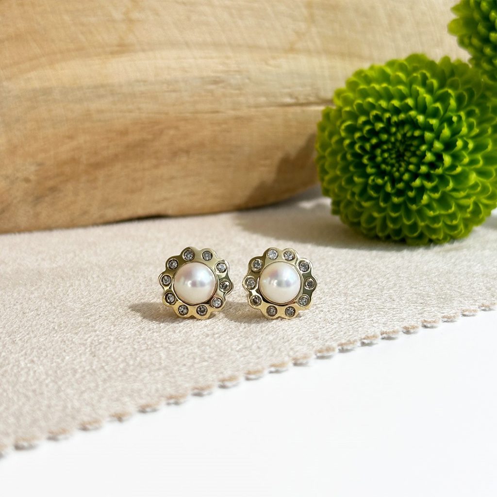 Perlenohrstecker mit Brillanten und Goldrand in floralem Design, präsentiert vor Holzhintergrund.