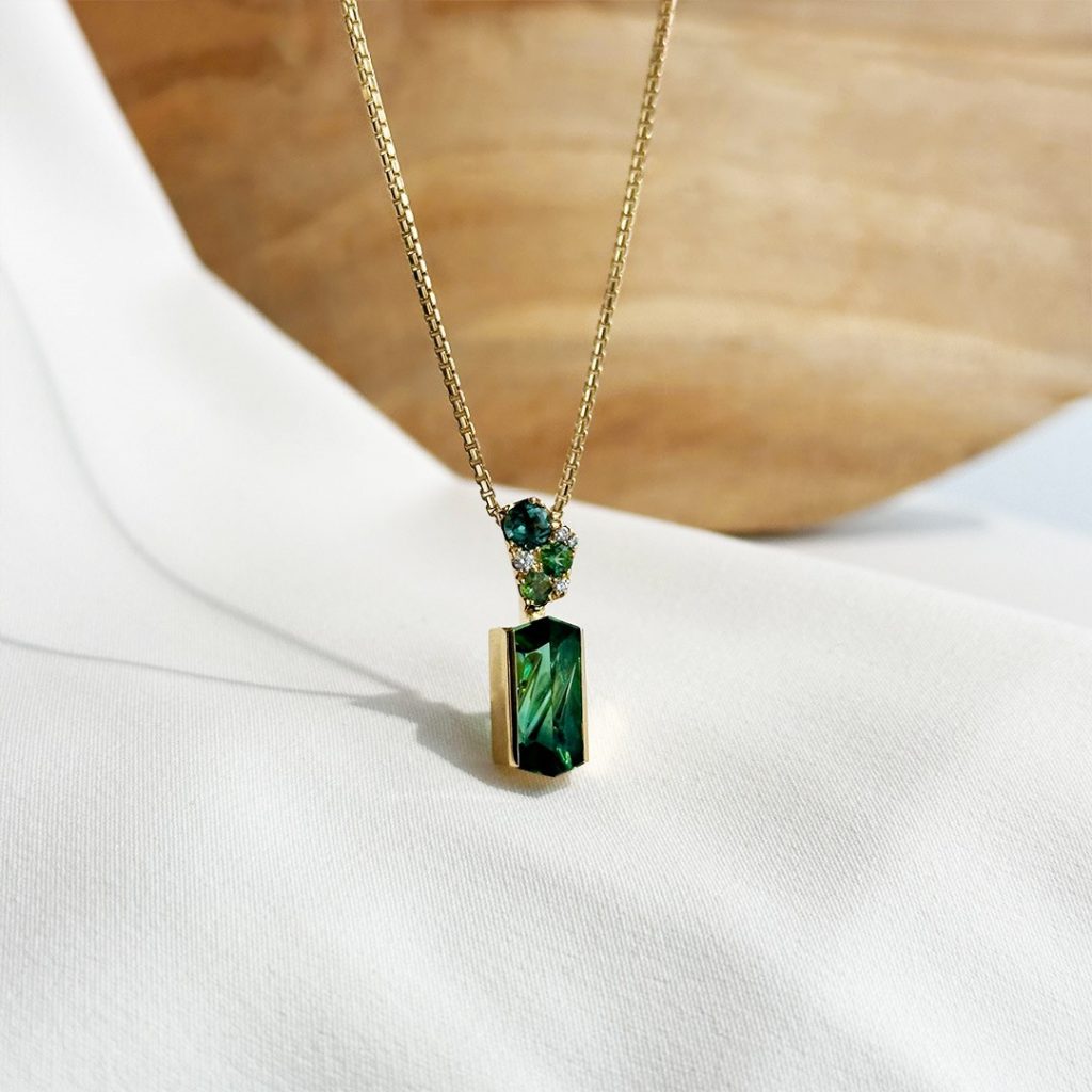 Handgefertigter Brillant-Turmalin-Anhänger in 585er Gelbgold an einer Venezianer Goldkette, präsentiert vor heller Holzwand.