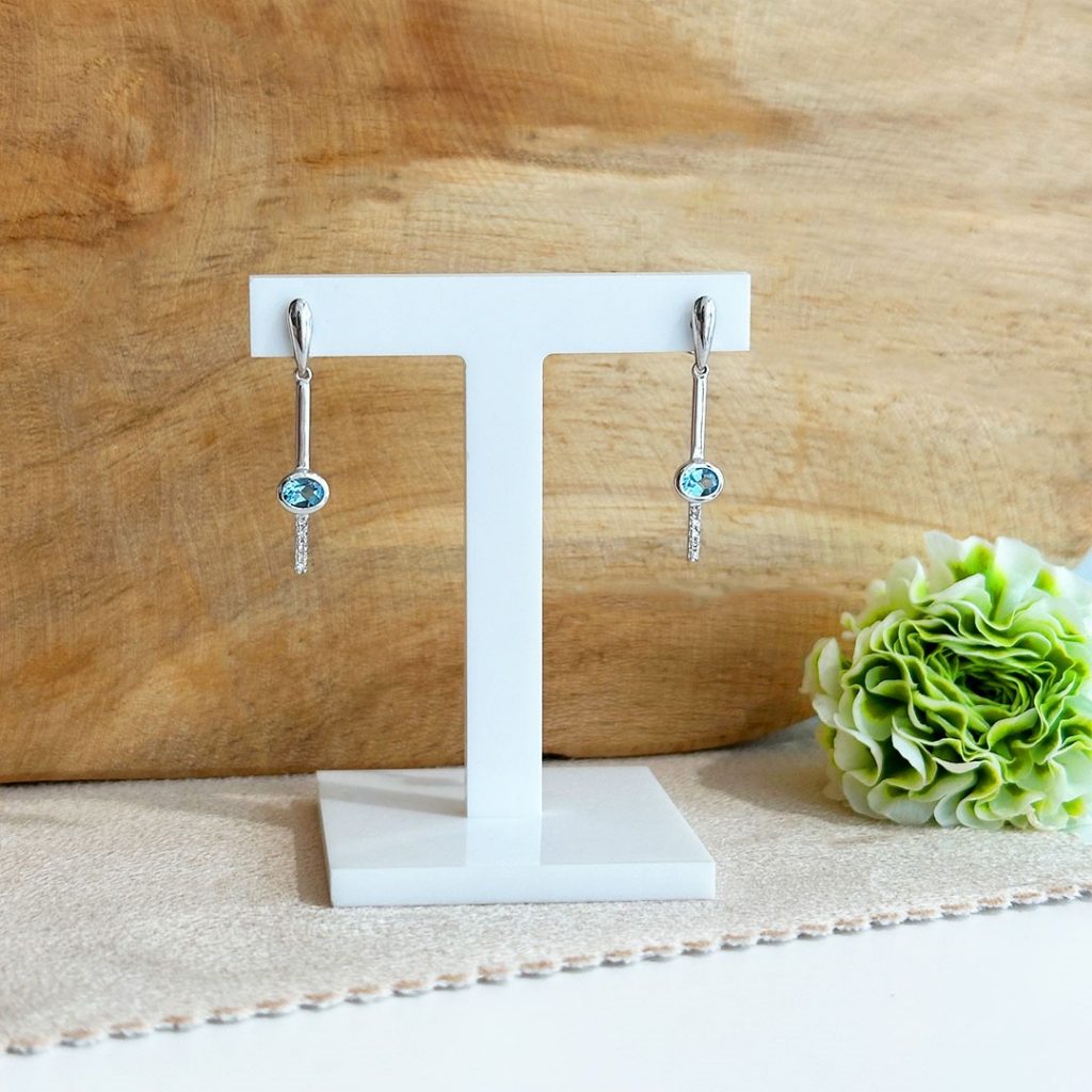 Elegante 585 Weißgold-Ohrringe mit Blautopas und 0,03 ct Diamanten, stilvoll vor Holzwand präsentiert. Artikelnummer 192