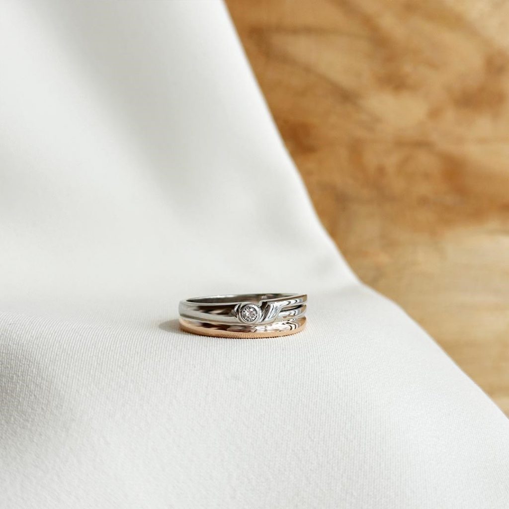 Eleganter Ring aus 585er Weiß- und Roségold mit 0,04ct. Brillant, präsentiert vor einer eleganten, hellen Holzwand. Artikelnummer 16457